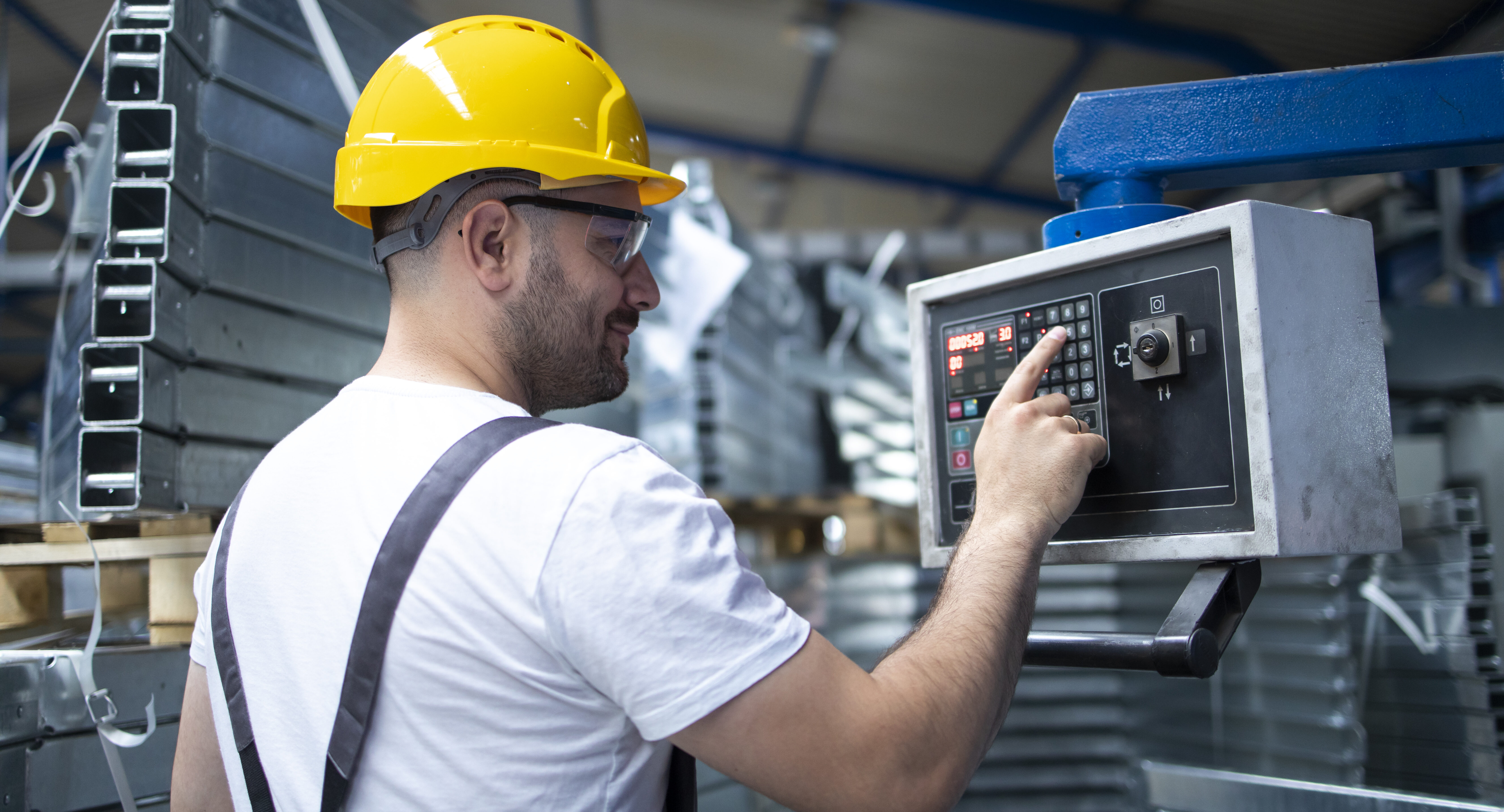 Factory worker in yellow hard hat operating industrial control panel for AI predictive maintenance system